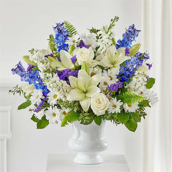 White lilies, roses, daisies, and blue flowers in a white vase