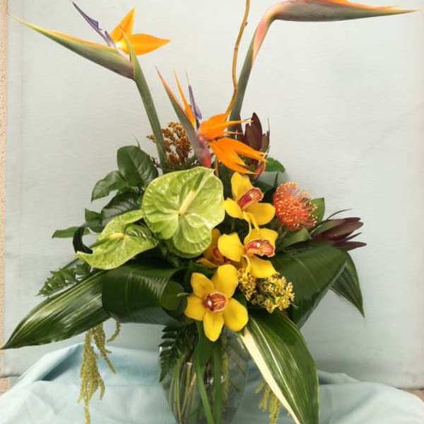 Tropical flower arrangement with orange bird-of-paradise and yellow orchids in a glass vase