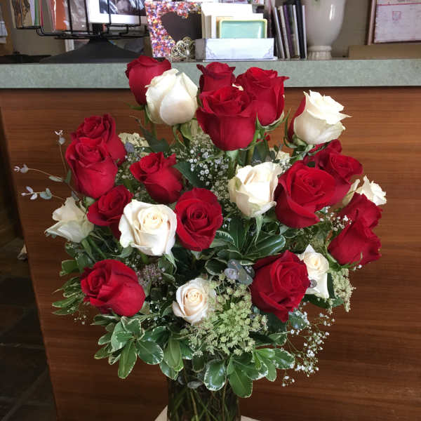 Red and white roses arranged in a clear glass vase with a red ribbon.
