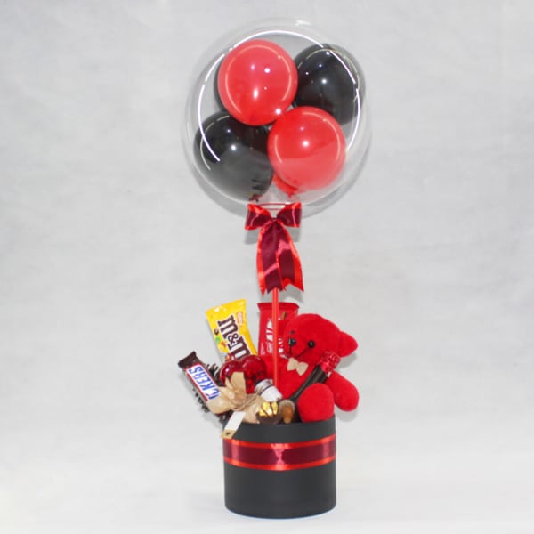 Balloon bouquet with red and black balloons, candy, and a red teddy bear in a black box