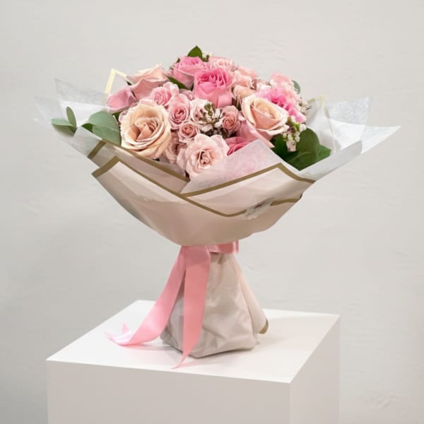 Pink and blush rose bouquet wrapped in pale paper with a pink ribbon