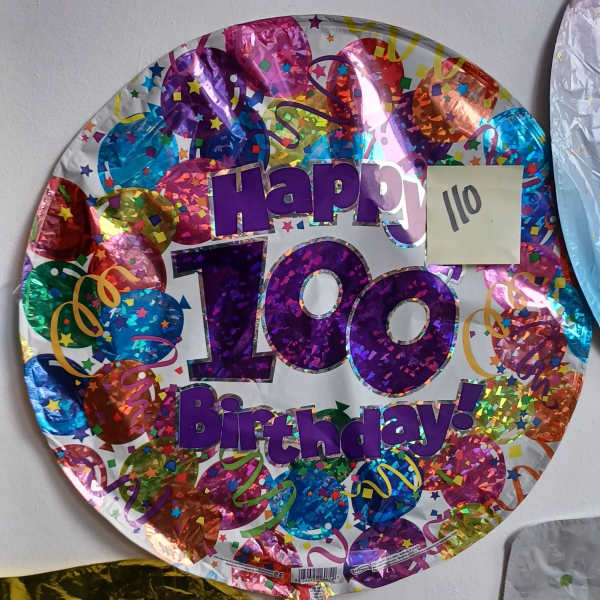 Round foil balloon reading Happy 100 Birthday with colorful confetti pattern