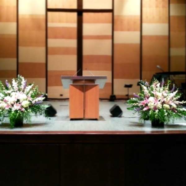 Two large pink, white, and purple altar arrangements flanking a wooden podium on a stage