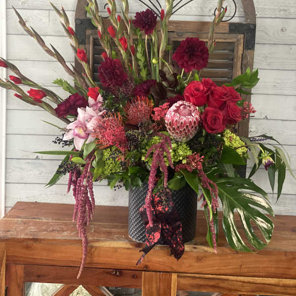 Large mixed floral arrangement in a black vase with red and pink blooms