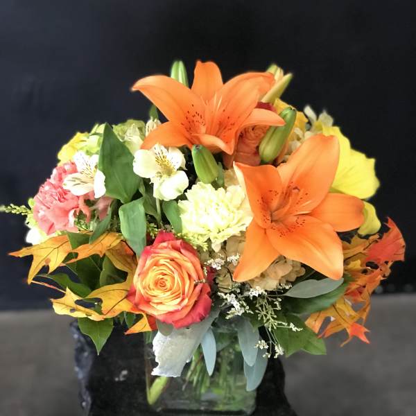 Orange lilies and roses in a glass vase with autumn leaves
