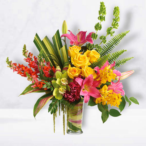 Bright mixed bouquet with yellow roses, pink lilies, and orchids in a glass vase