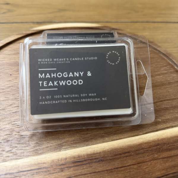 Clamshell candle package labeled Mahogany & Teakwood on a wooden tray