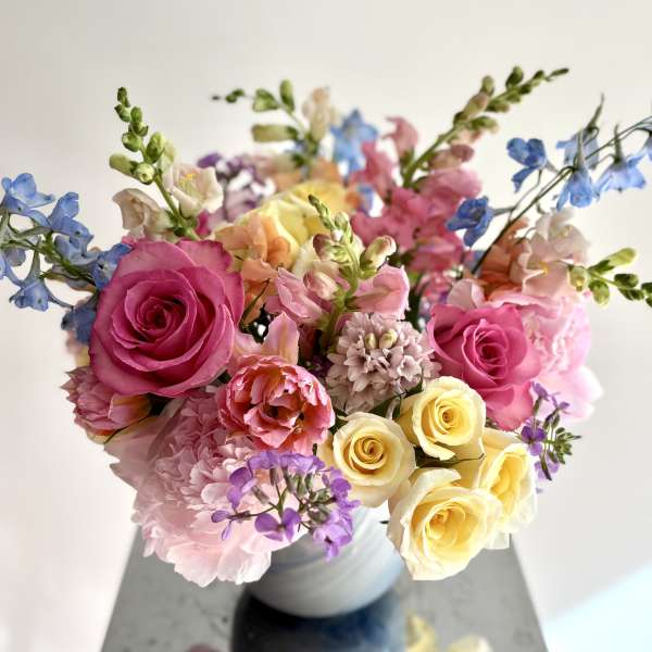 Mixed bouquet of pink, yellow, and blue flowers in a white vase
