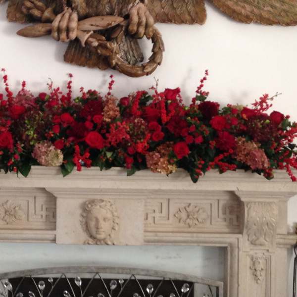 Long red floral arrangement displayed across a mantel