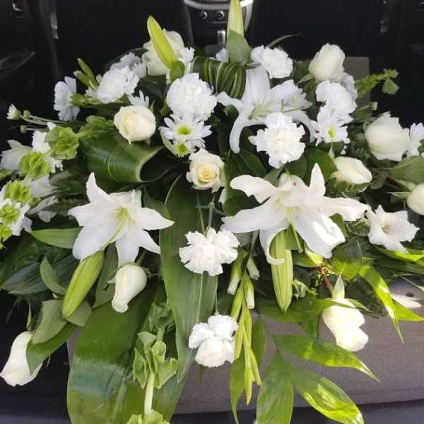 White floral casket spray with lilies, roses, and carnations