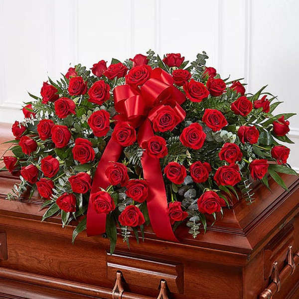 Red rose casket spray with a red ribbon on a wooden casket