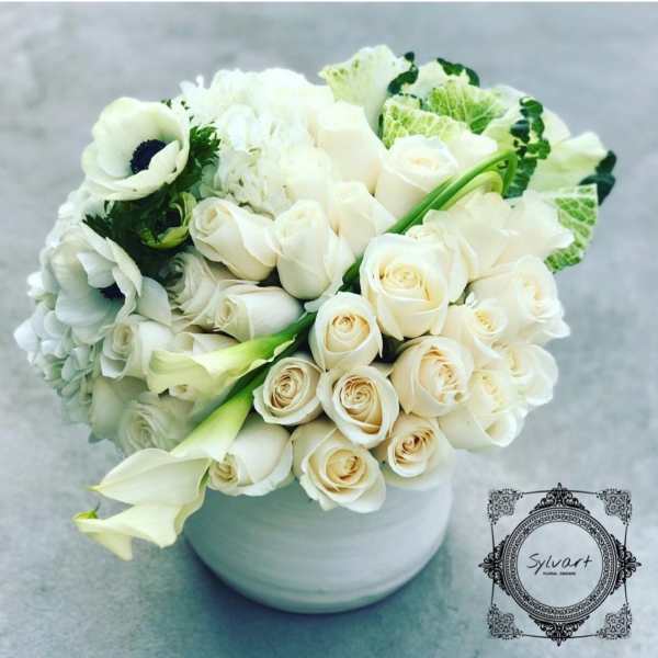 White roses and calla lilies arranged in a round white vase