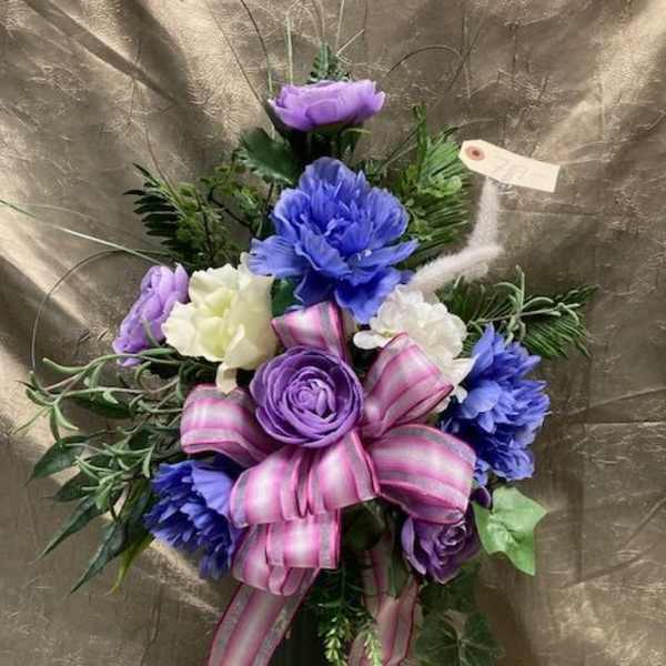Purple and white floral arrangement in a black vase with a pink ribbon