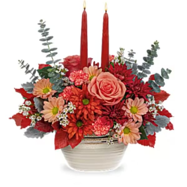 Red and peach floral arrangement in a white bowl with two red candles
