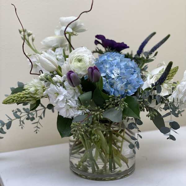 Mixed bouquet in a clear glass vase with blue hydrangea, white blooms, and purple tulips