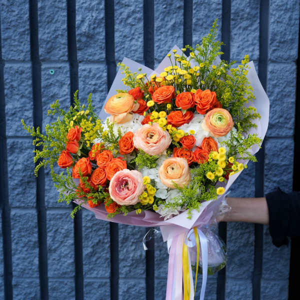 Bouquet of orange and peach flowers with yellow accents wrapped in pastel paper