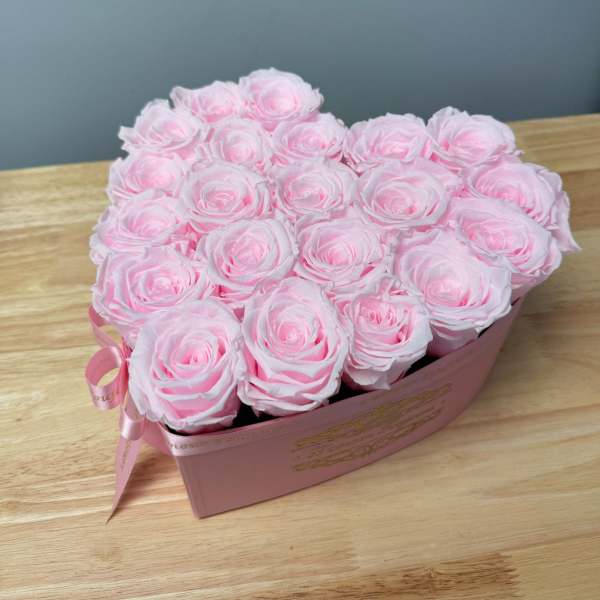 Heart-shaped pink box filled with light pink roses on a wooden surface