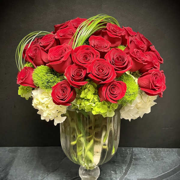 Tall arrangement of red roses with white and green blooms in a clear pedestal glass vase