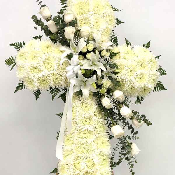 White floral cross arrangement on an easel with lilies and roses