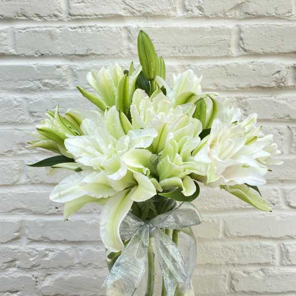 White lilies in a clear glass vase with a silver ribbon