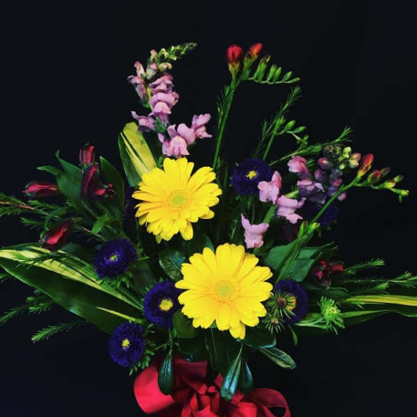 Bouquet of yellow daisies, purple blooms, and pink flowers with a red ribbon