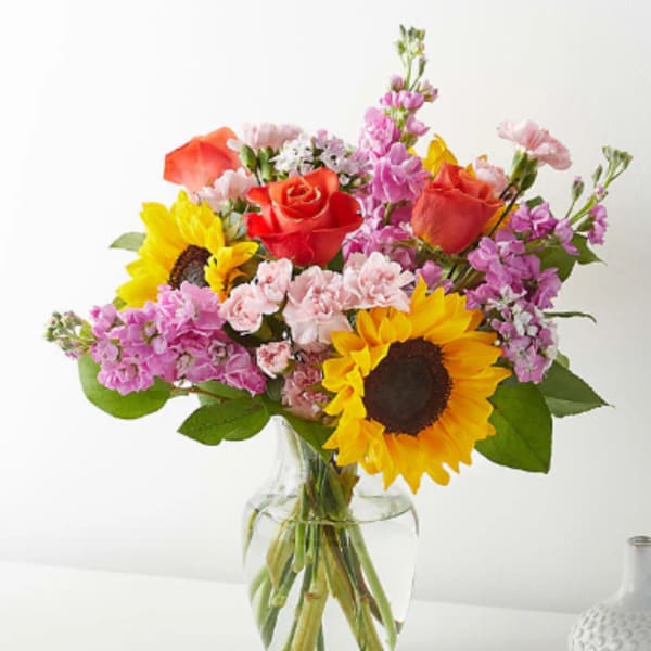 Bouquet of sunflowers, roses, and pink flowers in a clear glass vase