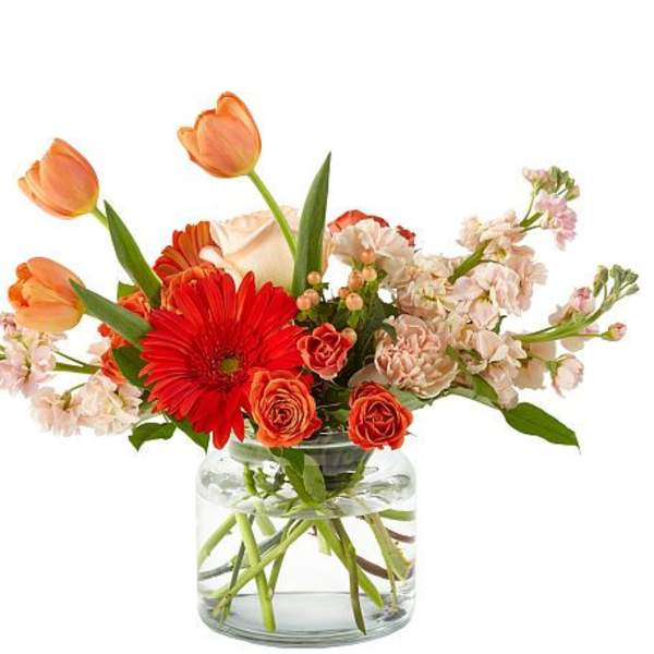 Mixed bouquet of orange tulips, red gerbera daisies, and peach roses in a glass vase