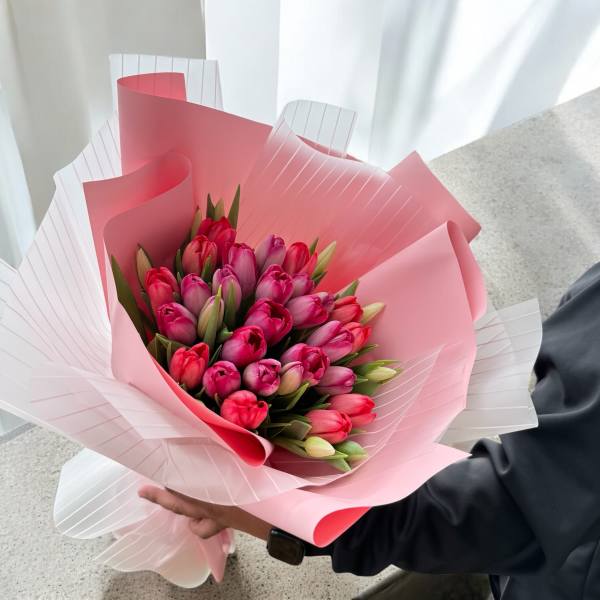Handheld bouquet of pink and magenta tulips wrapped in pink paper