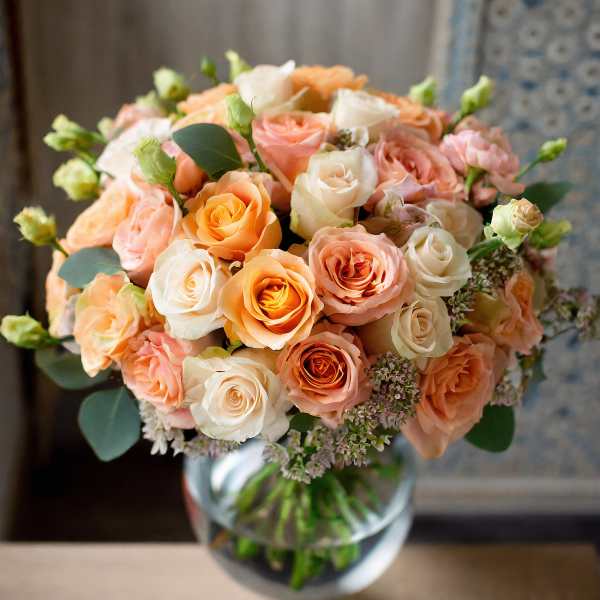 Peach and white roses arranged in a clear glass vase