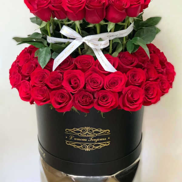 Two tiers of red roses in a black hatbox with a white ribbon