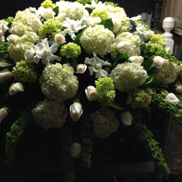 Large white floral casket spray with hydrangeas, roses, and calla lilies