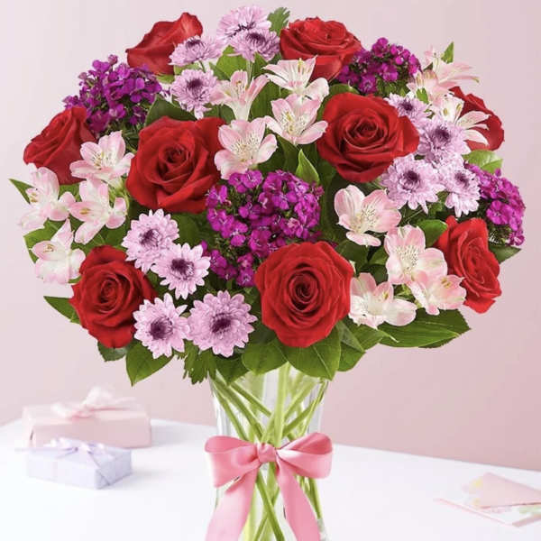 Bouquet of red roses and pink flowers in a glass vase with a pink ribbon