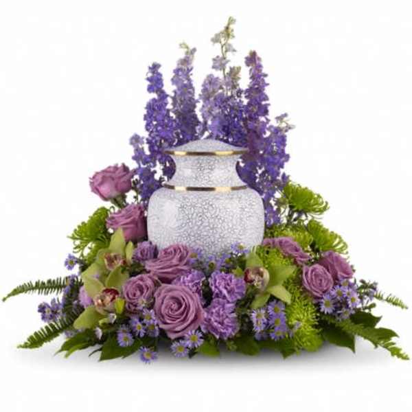 Purple floral arrangement around a white urn with gold trim