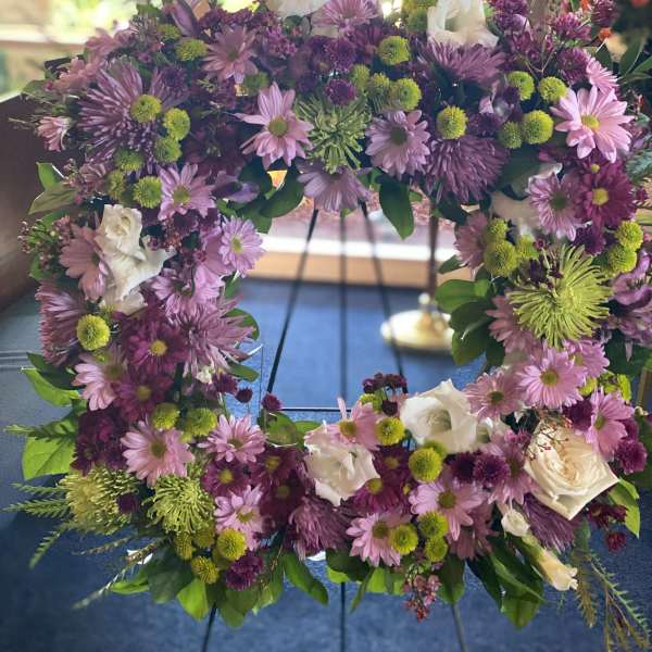 Purple and pink floral wreath with white roses on a stand