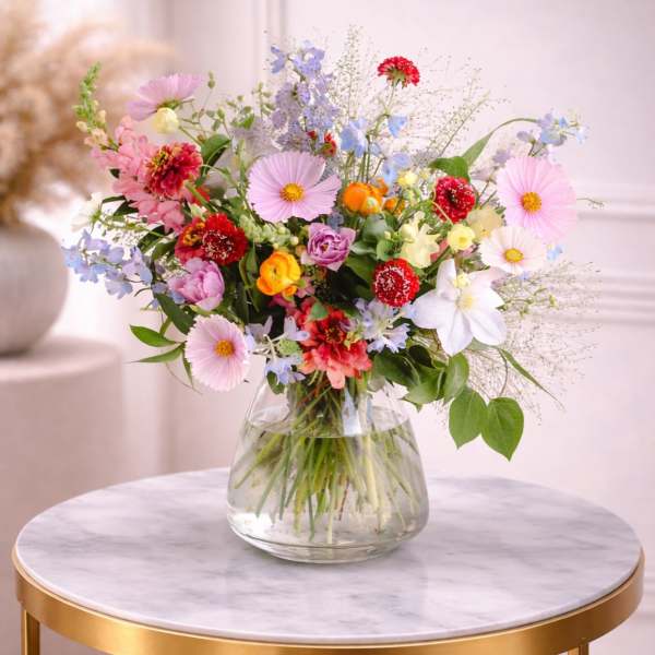 Colorful mixed spring flower arrangement in a clear glass vase on a marble-topped gold table