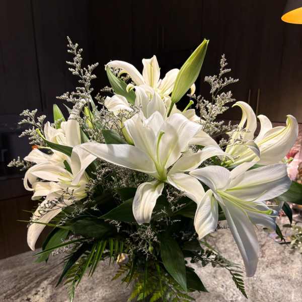 White lilies arranged in a glass vase with greenery