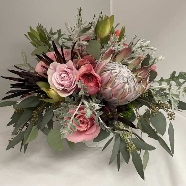 Pink roses and a protea in a low white container