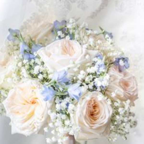 Blush and white rose bouquet in a glass vase with small blue flowers
