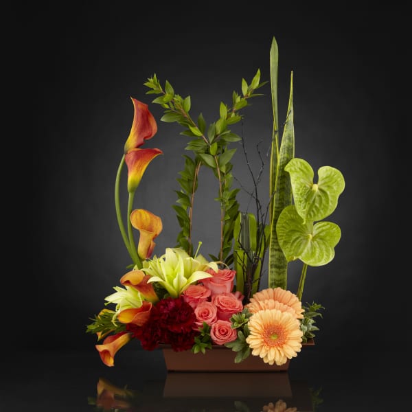 Mixed floral arrangement with calla lilies, roses, and gerbera daisies in a rectangular vase