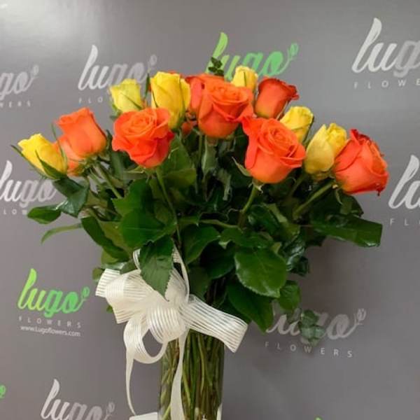 Bouquet of orange and yellow roses in a clear glass vase with a white ribbon