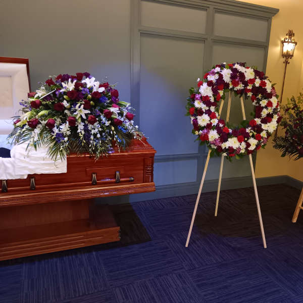 Funeral casket spray, standing wreath, and floral vase arrangement in red, white, and purple