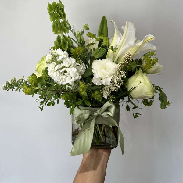 White floral arrangement in a glass vase with a green ribbon