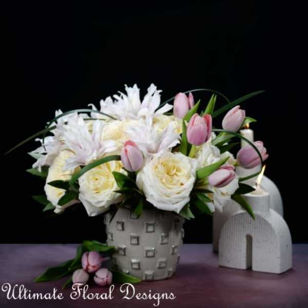 White and pink floral arrangement in a patterned vase with candles nearby