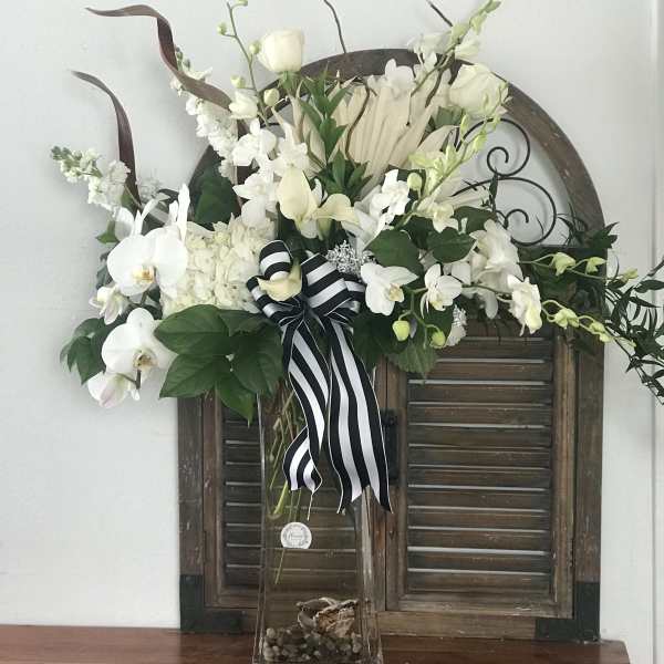 White orchid and rose arrangement in a tall glass vase with a striped ribbon