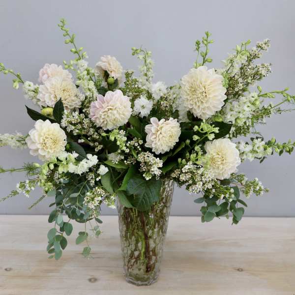 Tall arrangement of cream dahlias and white flowers in a clear textured glass vase