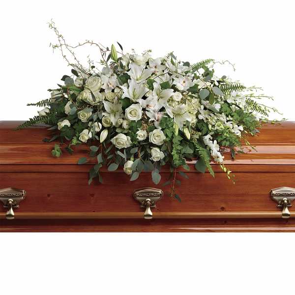 White casket spray of lilies, roses, and orchids on a polished wood casket