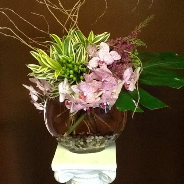 Pink orchids arranged in a round glass vase with decorative branches.