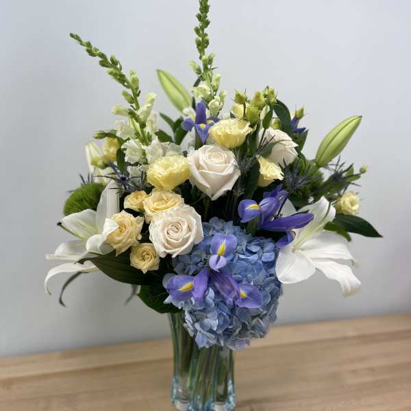 Bouquet of white roses, blue hydrangea, and purple irises in a glass vase