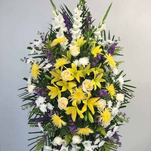 Tall funeral spray with yellow lilies, white roses, and purple accents