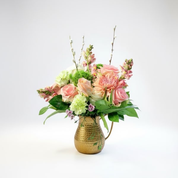 Pink and peach flowers arranged in a gold pitcher vase